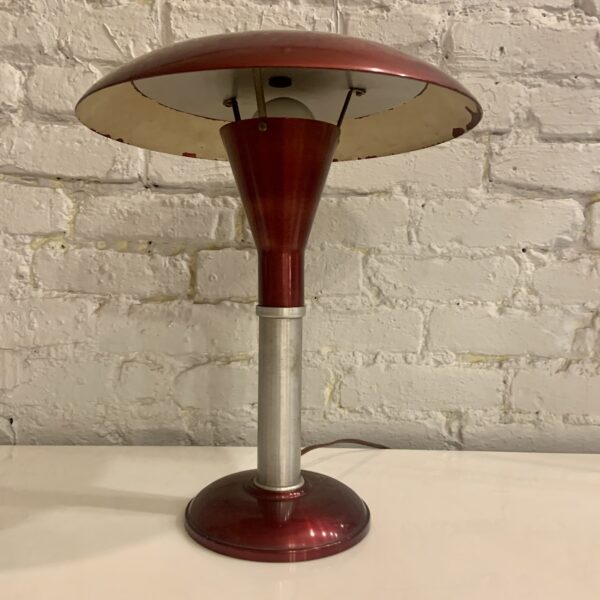 The Art Deco/Machine Age, Mid-Century Mooncrest sight light table lamp is an icon of American Post-War design. It was manufactured by the Smith Metal Arts Company of Buffalo, NY and incorporates designer, Laurence E. Corcoran's patented aluminum indirect reflector under the shade. This design was produced in several colorways and this particular example of this famous lamp is in a rich burgundy and silver anodized finish. Under the shade it has the Mooncrest logo decal and the words patent applied for and under the reflector has the period underwriters approval decal containing the Smith Metal Arts credit. This iconic lamp is in amazing all-original condition, retains its original felt to the underside of the base